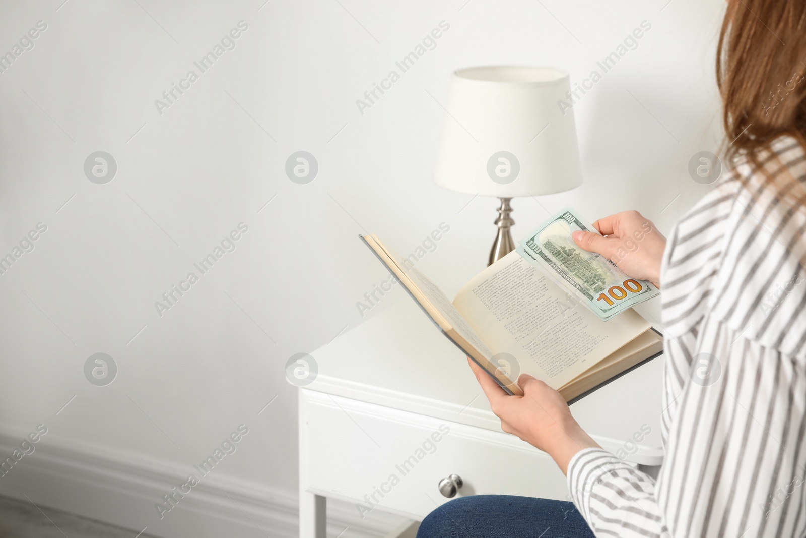 Photo of Woman hiding dollar banknotes in book indoors, closeup. Money savings