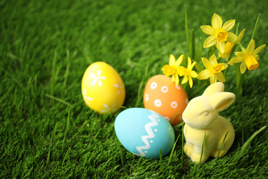 Colorful Easter eggs, rabbit and narcissus flowers in green grass