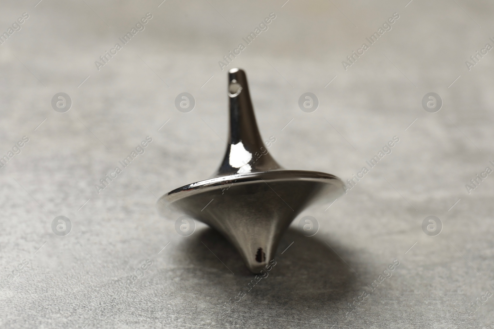 Photo of One silver spinning top on grey textured background, closeup