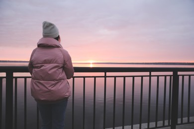 Woman standing near river at sunset, back view