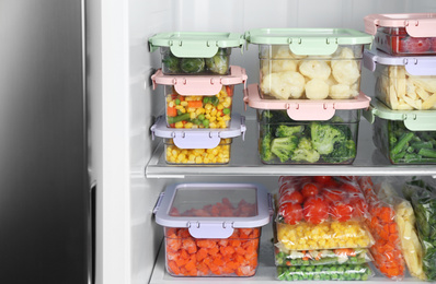 Plastic bags and containers with different frozen vegetables in refrigerator