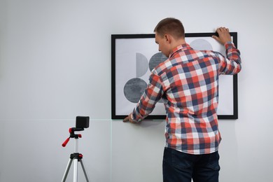 Man using cross line laser level for hanging painting on light wall, back view