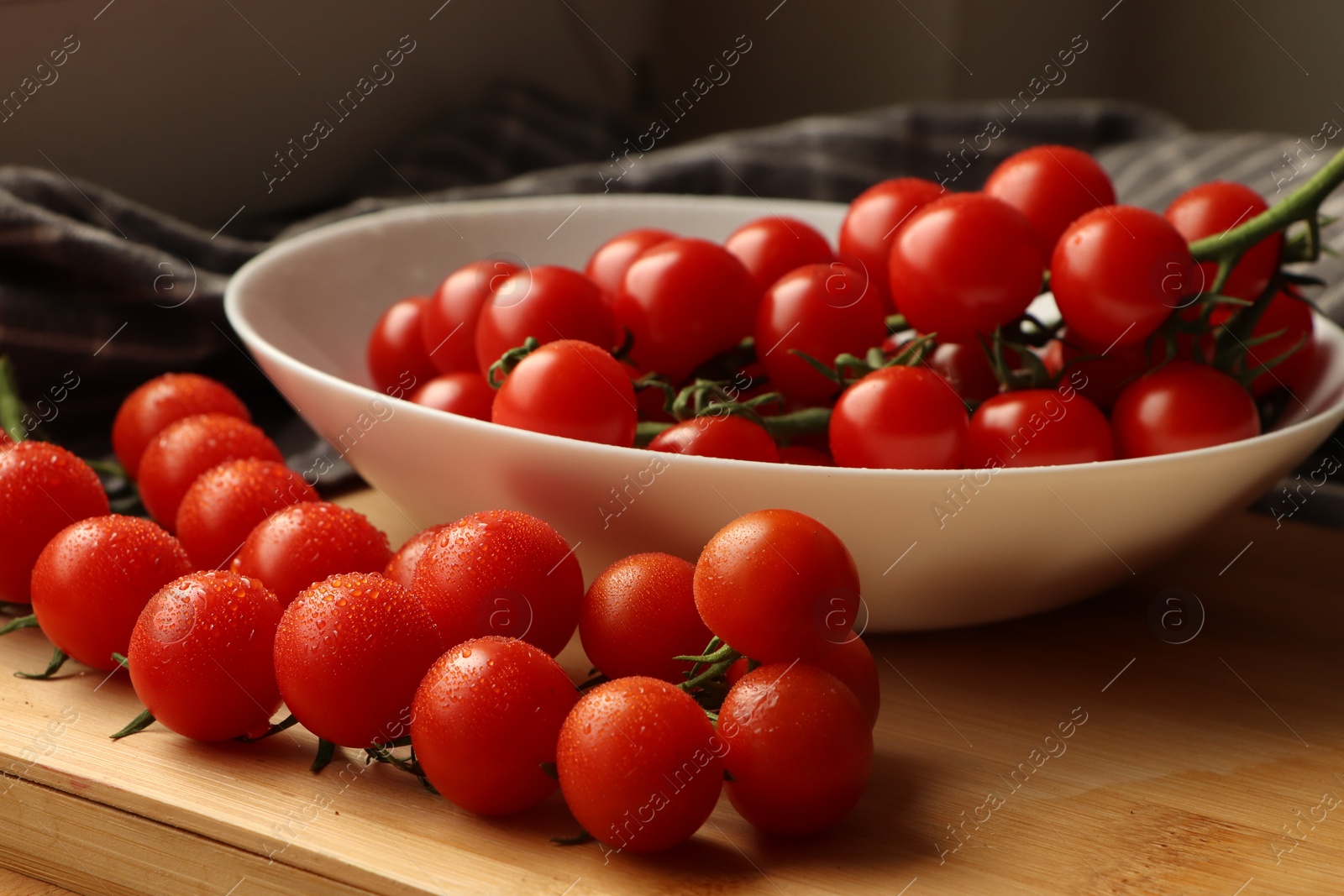 Photo of Plate of ripe whole cherry tomatoes with water drops on wooden table, closeup