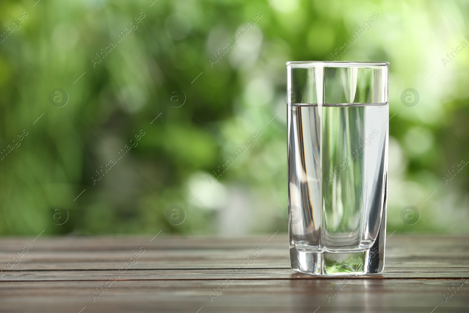 Photo of Glass of fresh water on wooden table outdoors. Space for text