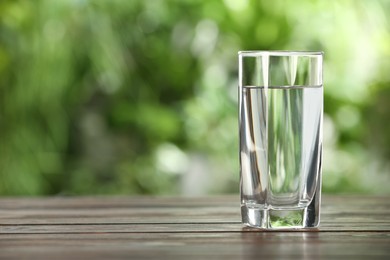 Glass of fresh water on wooden table outdoors. Space for text