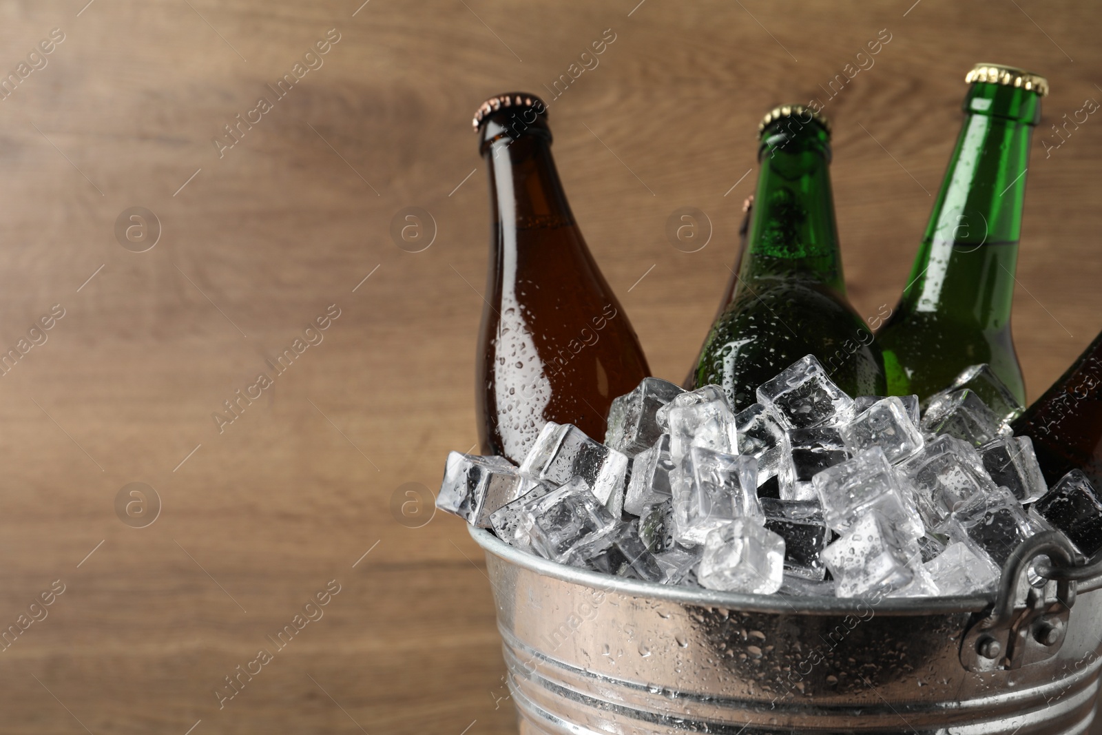 Photo of Metal bucket with beer and ice cubes on wooden background. Space for text