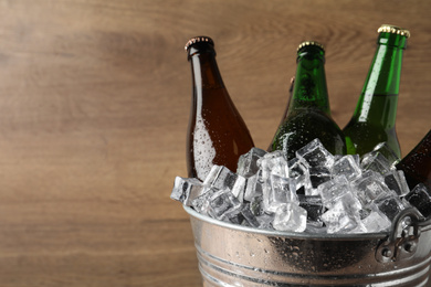 Photo of Metal bucket with beer and ice cubes on wooden background. Space for text