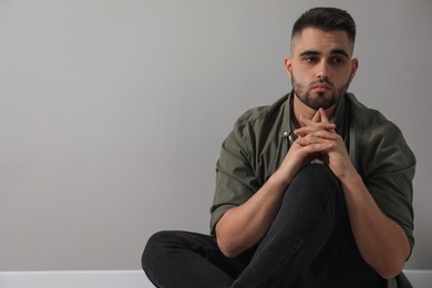 Sad man sitting near light grey wall. Space for text