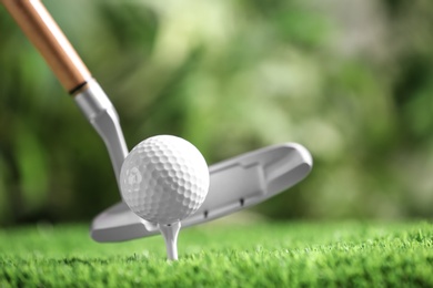 Photo of Hitting golf ball with club on artificial grass against blurred background, space for text