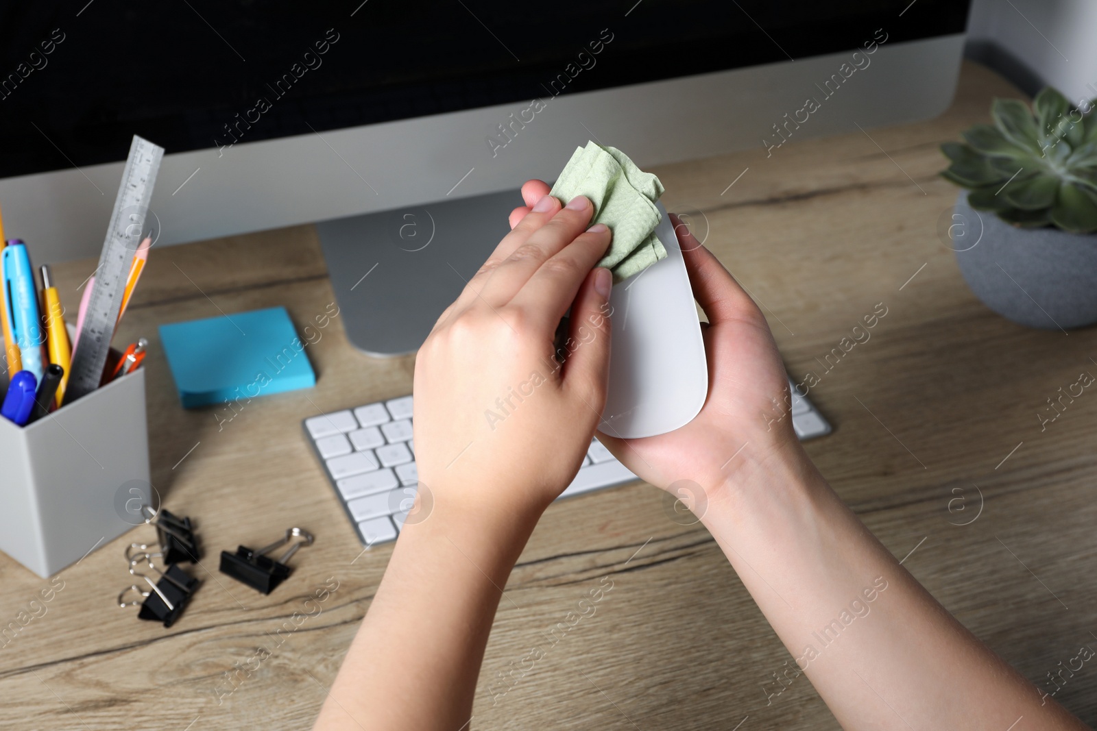Photo of Woman wiping wireless mouse with paper towel near wooden table, closeup