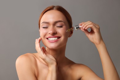 Photo of Beautiful young woman applying cosmetic serum onto her face on grey background
