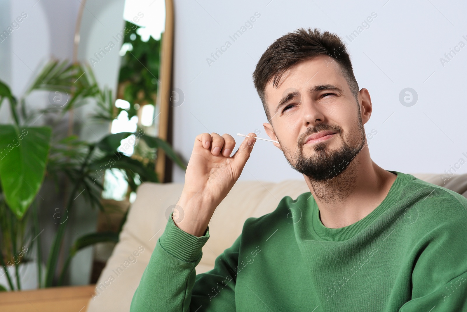 Photo of Young man cleaning ear with cotton swab at home. Space for text