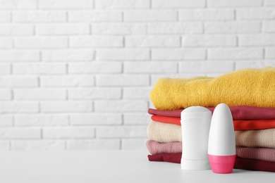 Deodorants near stack of clean clothes on white table. Space for text