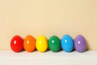 Photo of Easter eggs on white wooden table against beige background, space for text