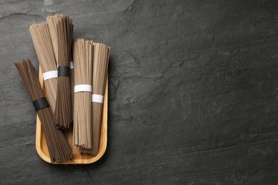 Photo of Uncooked buckwheat noodles (soba) on black table, top view. Space for text