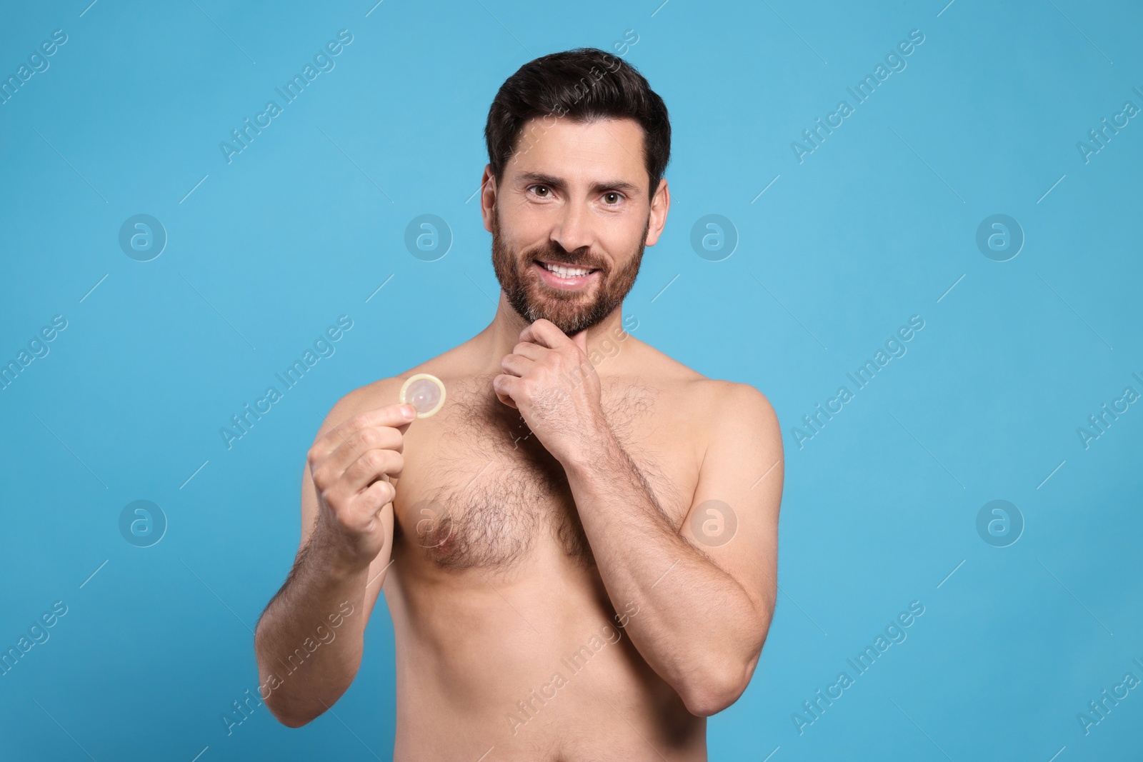 Photo of Naked man holding condom on light blue background. Safe sex