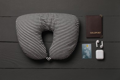 Photo of Striped travel pillow, passport, credit card and earphones on black wooden background, flat lay