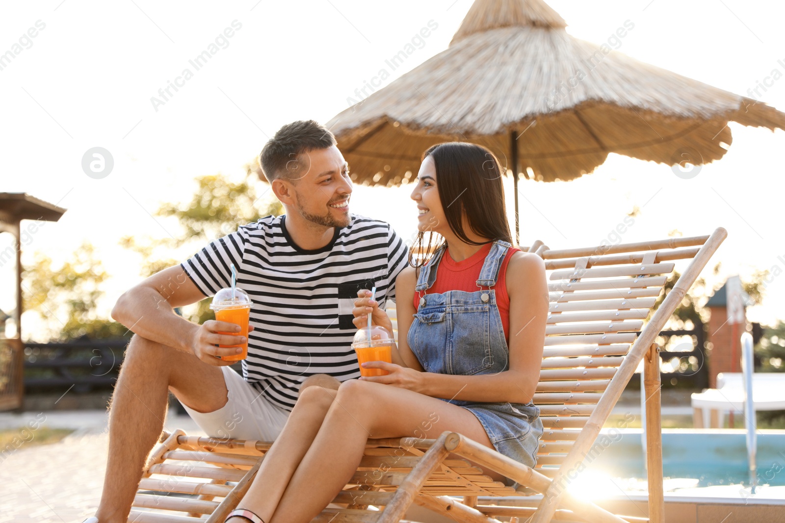 Image of Happy couple with cups of refreshing drink resting in deck chairs outdoors