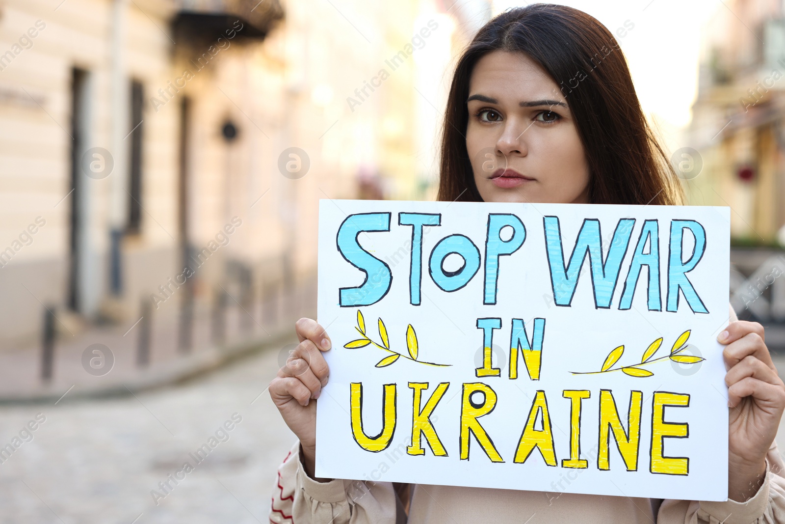 Photo of Sad woman holding poster Stop War in Ukraine on city street. Space for text