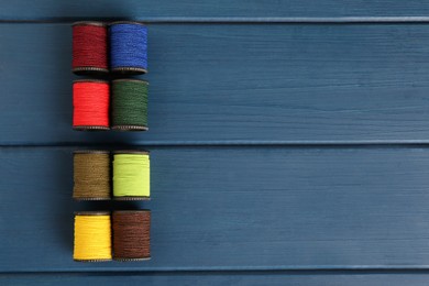Set of color sewing threads on blue wooden table, flat lay. Space for text