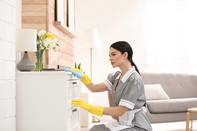 Photo of Young chambermaid wiping dust from furniture in hotel room