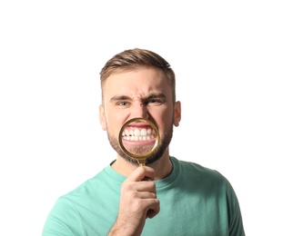 Young man with healthy teeth and magnifier on white background