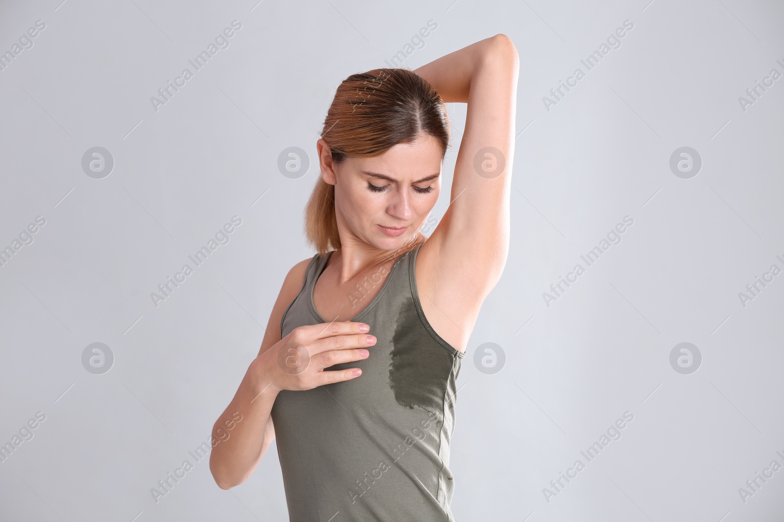 Photo of Young woman with sweat stain on her clothes against light background. Using deodorant