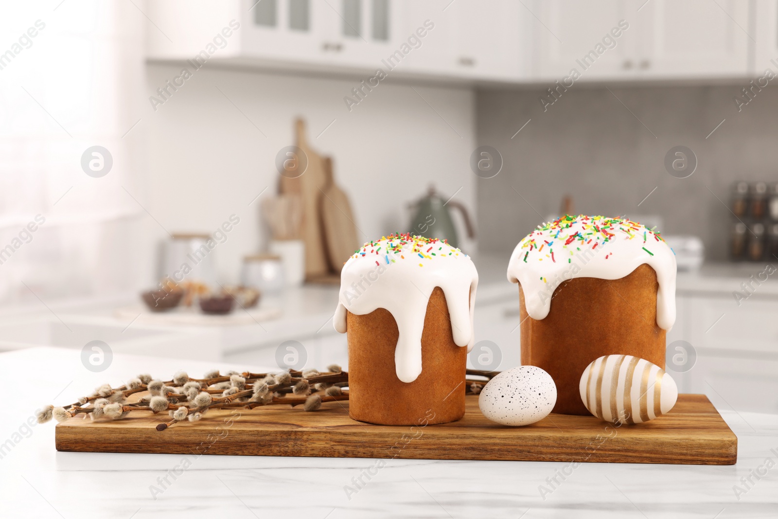 Photo of Delicious Easter cakes with sprinkles, decorated eggs and willow branches on white table in kitchen. Space for text
