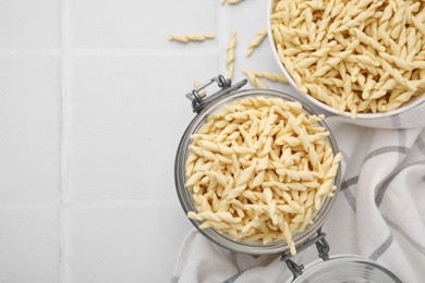 Uncooked trofie pasta on white tiled table, flat lay. Space for text