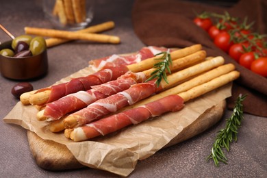 Photo of Delicious grissini sticks with prosciutto and ingredients on brown textured table