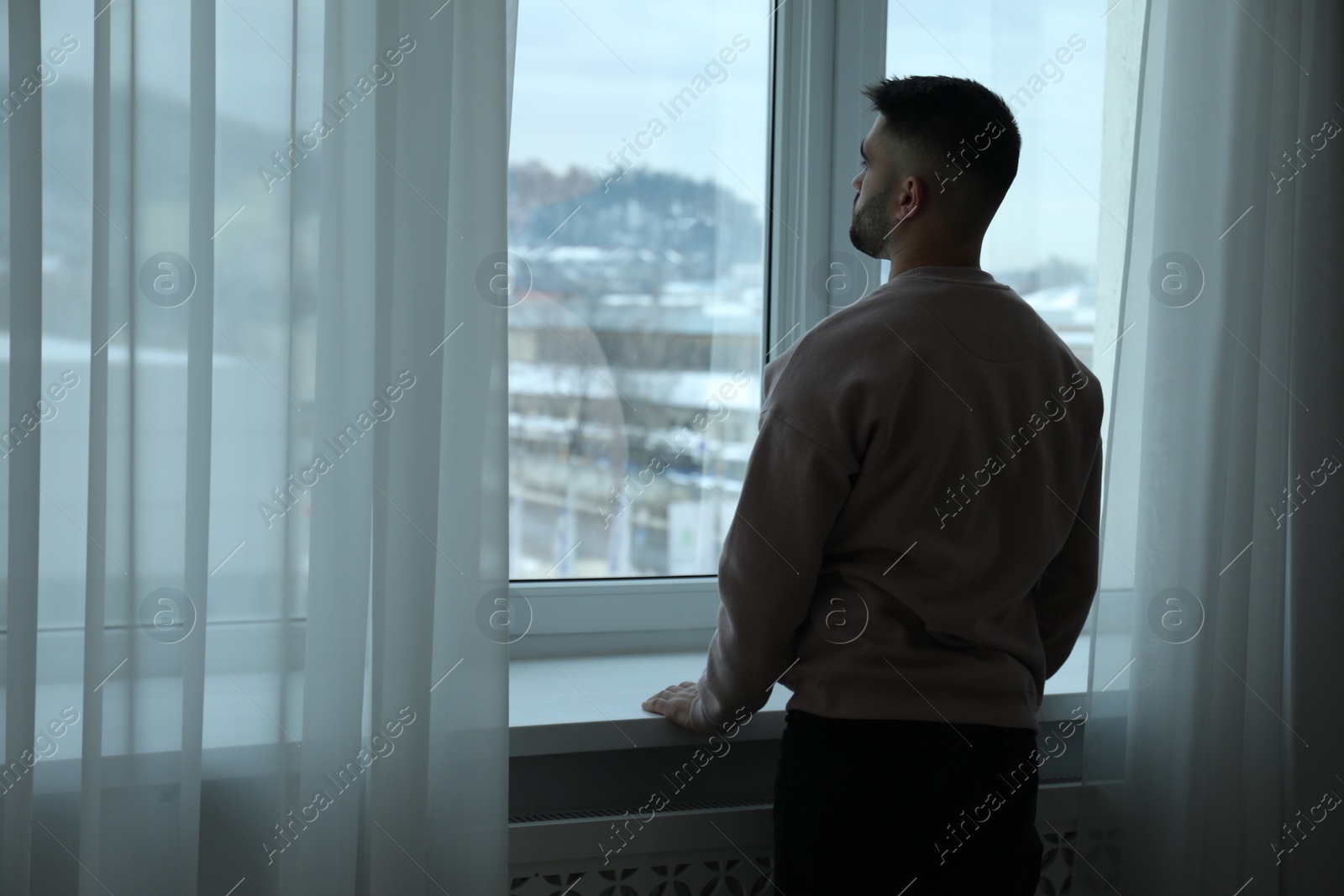 Photo of Sad man looking at window at home, back view. Space for text