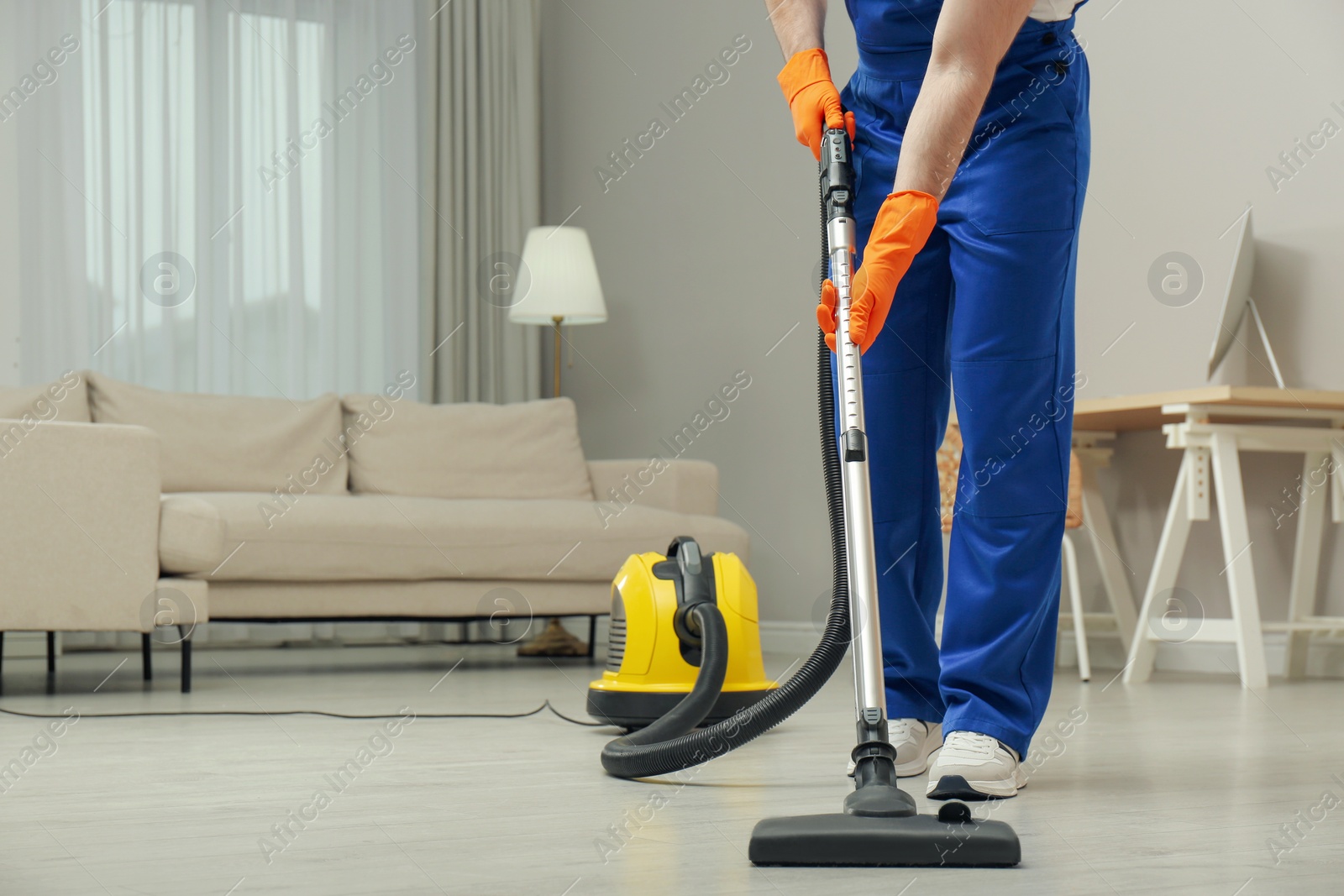 Photo of Janitor in uniform vacuuming floor indoors, closeup. Space for text