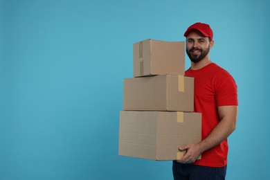 Photo of Happy courier with stack of parcels on light blue background, space for text