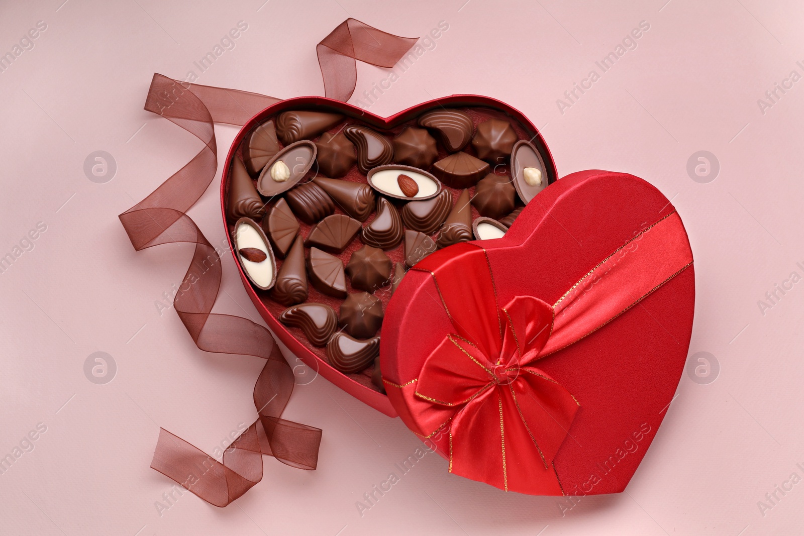 Photo of Heart shaped box with delicious chocolate candies and ribbon on pale pink background, flat lay