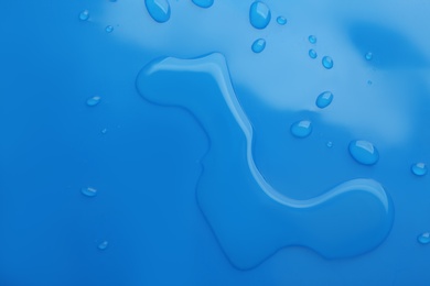 Photo of Drops of spilled water on blue background, top view
