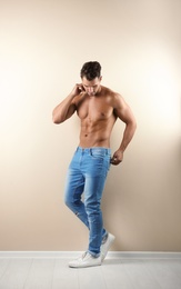 Photo of Shirtless young man in stylish jeans near light wall