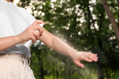 Photo of Woman applying insect repellent on arm in park, closeup. Tick bites prevention