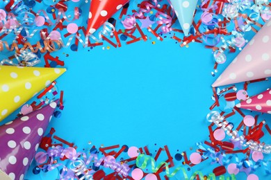 Frame of colorful serpentine streamers, party hats and confetti on light blue background, flat lay. Space for text