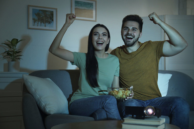 Emotional young couple watching TV using video projector at home
