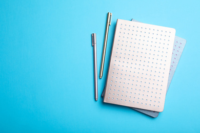 Photo of Stylish notebooks and pens on light blue background, flat lay. Space for text