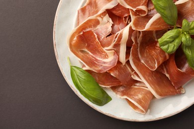 Photo of Slices of tasty cured ham and basil on grey background, top view. Space for text