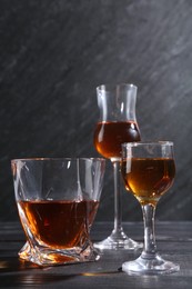 Photo of Different delicious liqueurs in glasses on black wooden table