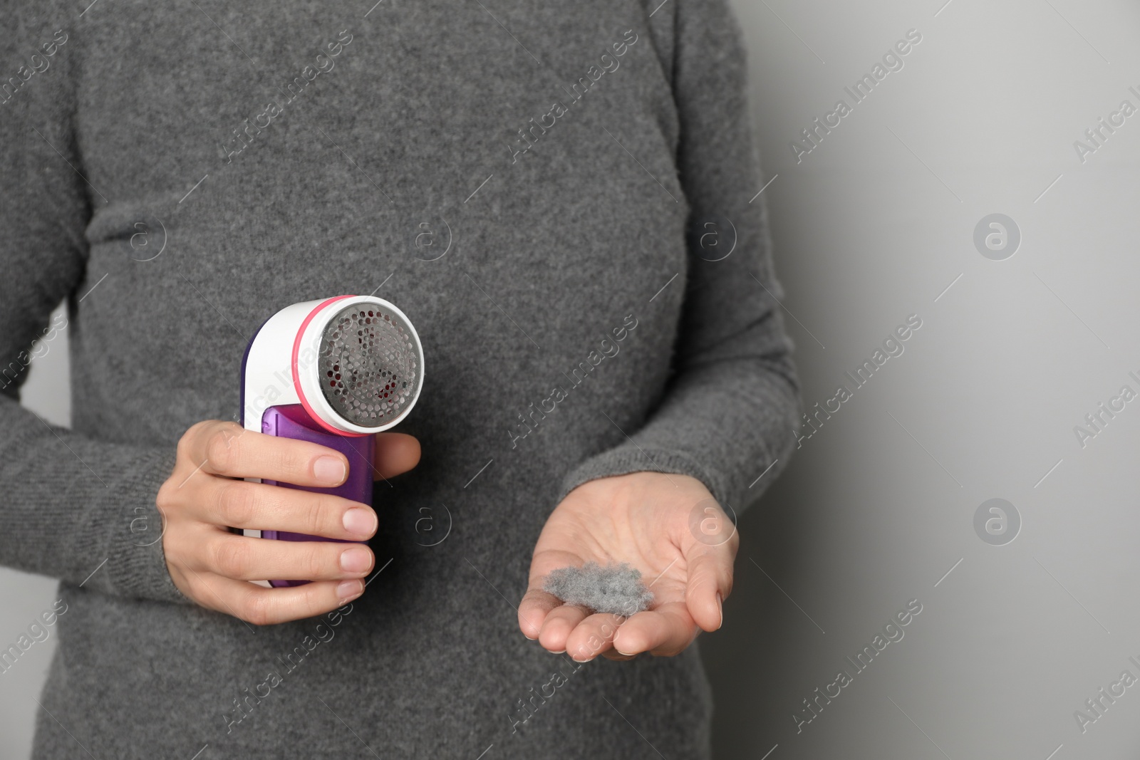 Photo of Woman in woolen sweater holding fabric shaver and lint on light grey background, closeup