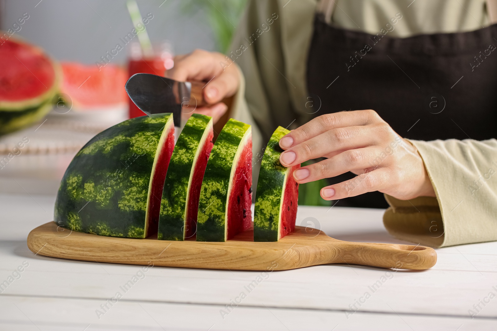 Photo of Woman cutting delicious watermelon at white wooden table indoors, closeup