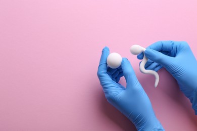 Photo of Reproductive medicine. Fertility specialist in gloves holding figures of sperm and egg cells on pink background, top view with space for text