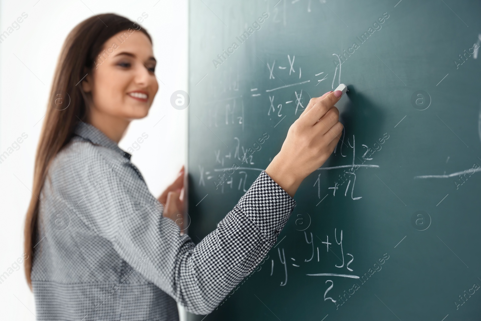 Photo of Young female teacher writing on blackboard in classroom