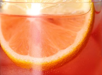 Glass of refreshing drink with ice cubes and lemon slice as background, closeup