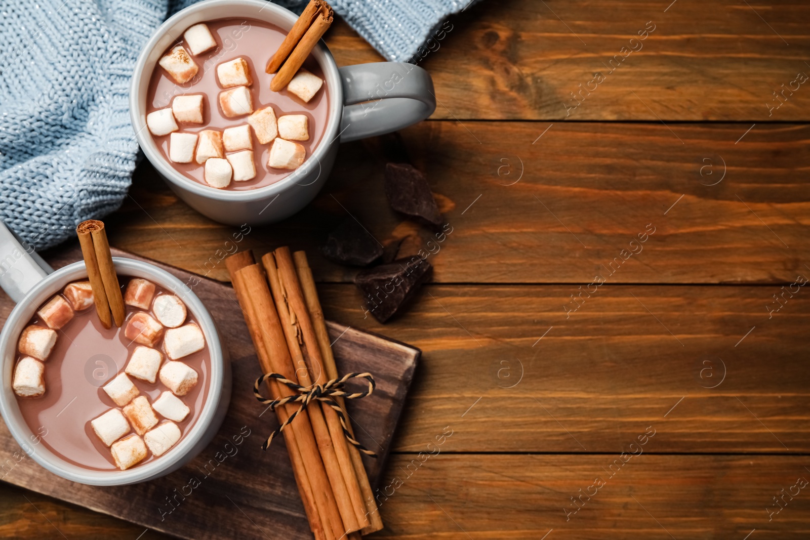 Photo of Delicious hot drinks with cinnamon and marshmallows on wooden table, flat lay. Space for text