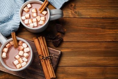 Delicious hot drinks with cinnamon and marshmallows on wooden table, flat lay. Space for text