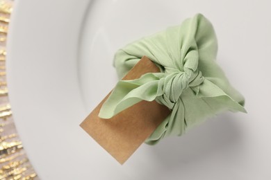 Photo of Furoshiki technique. Gift packed in green fabric with blank card on plate, top view